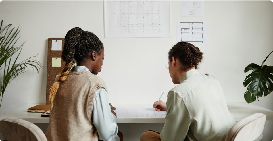 Black woman with braided pony tail wear a brown sweater vest with a white shirt talking to a White male coworker with curly brown hair wearing brown pants and light green shirt sitting in a conference room discussing using LegalZoom for their business dissolution.