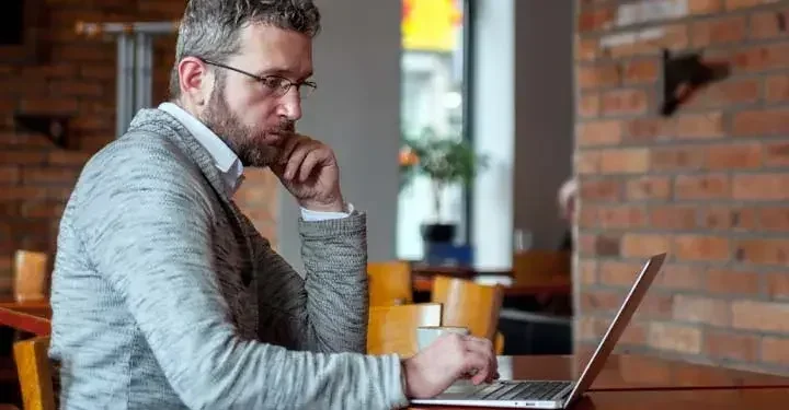 Man in café looking intently at laptop and reading about deed of trust and how to appoint a trustee while transfering his property.