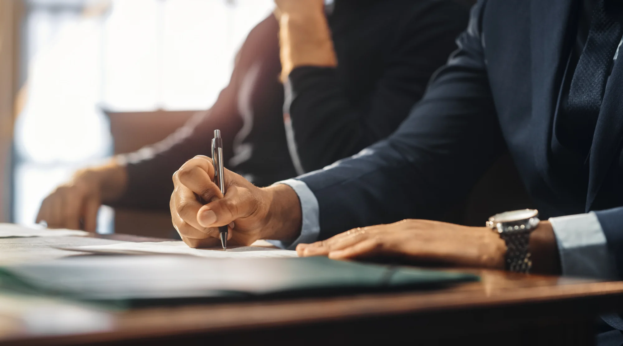 Close up of a man's hand signing a document at a desk.