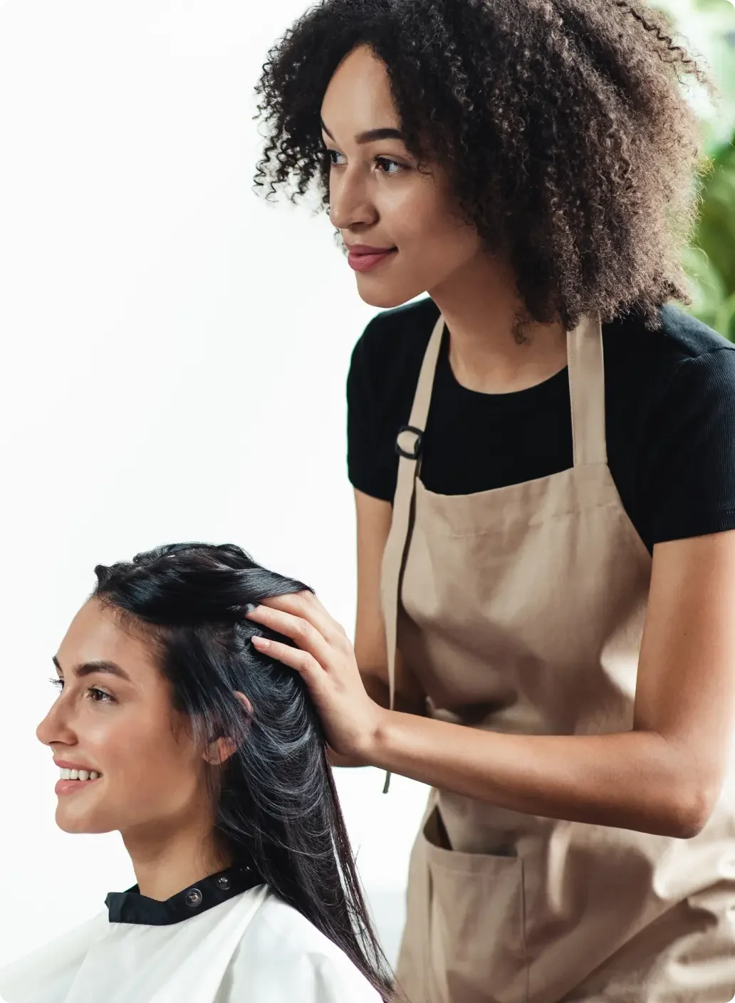 A woman wearing an apron who is styling another woman's hair.