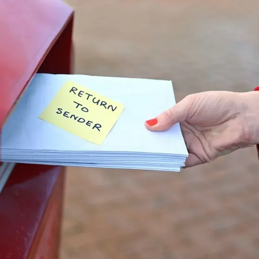 A hand with red nail polish mails a pile of letters marked "return to sender."