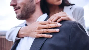 Close up of a woman's hand with her wedding ring visible, arms wrapped around her husband.