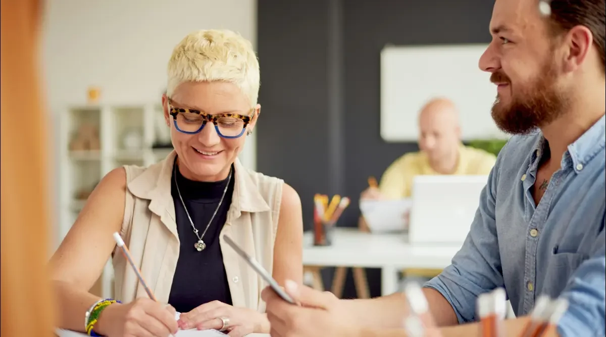 A woman and a man seated at a table discuss a slogan for their new business.