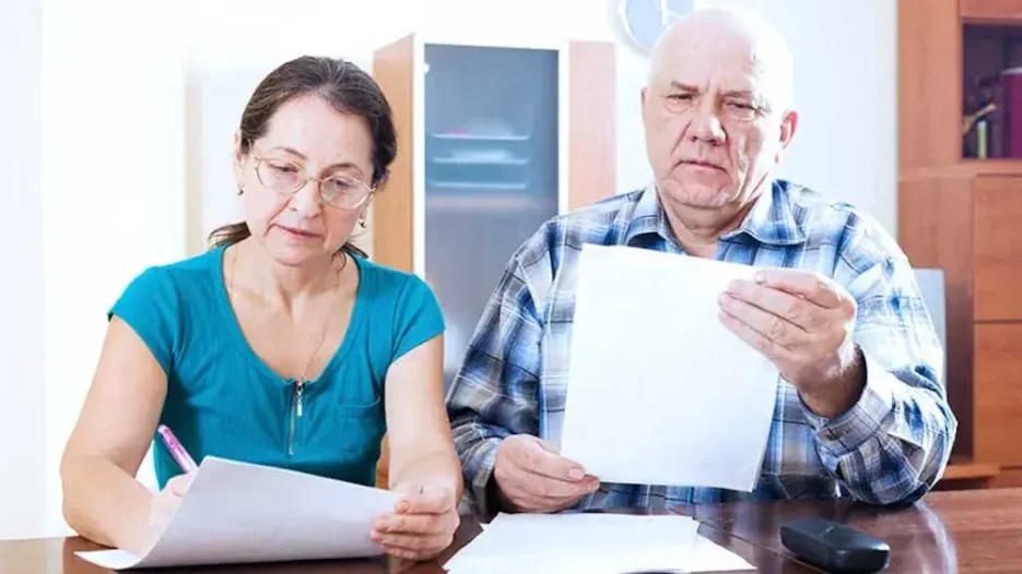An elderly couple sits closely at a table, comparing notes on living will versus last will and testament documents, thoughtfully deciding on estate planning options.