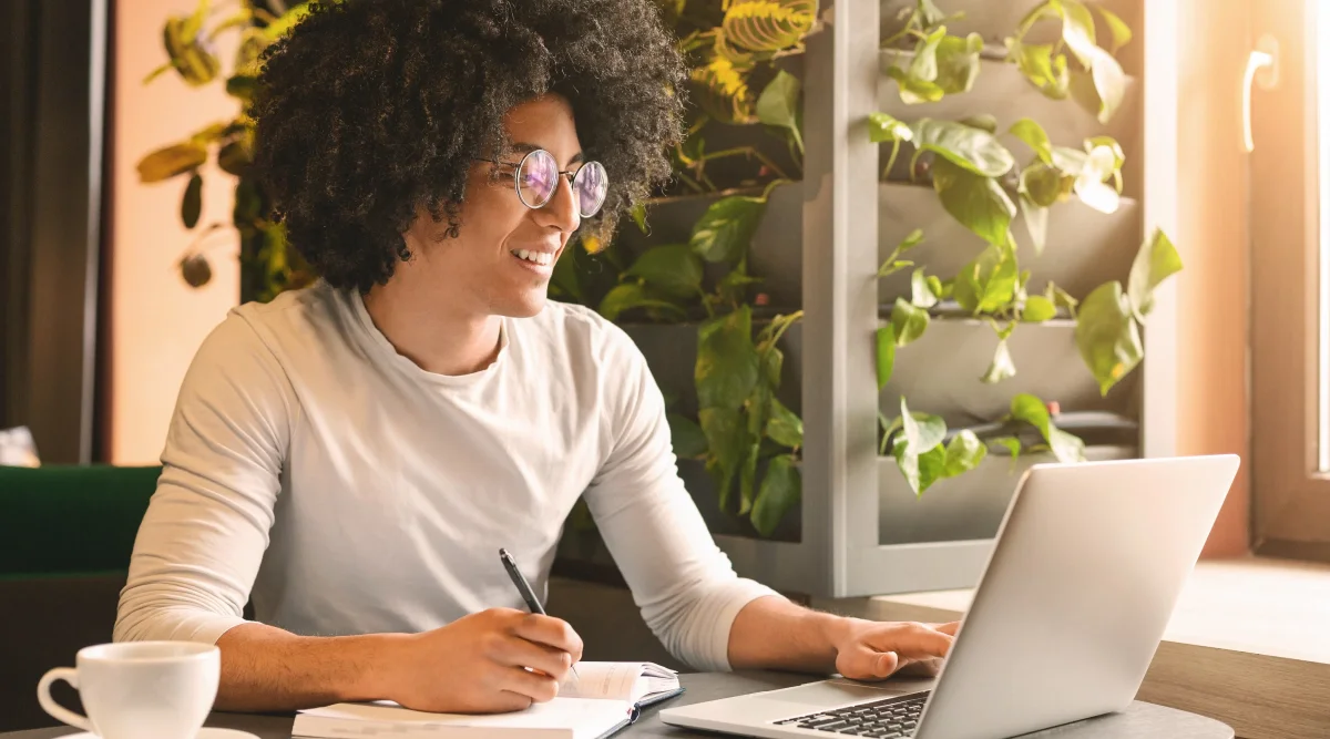 Smiling man in glasses using a laptop by a green wall