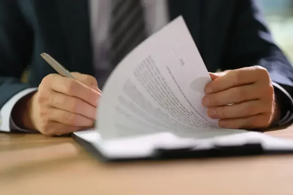 A man wearing a professional suit, reading a durable power of attorney (DPOA) documentation, and signing it to be submitted for further processing.