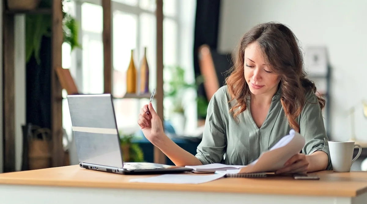 Woman reviewing papers at a desk with a laptop