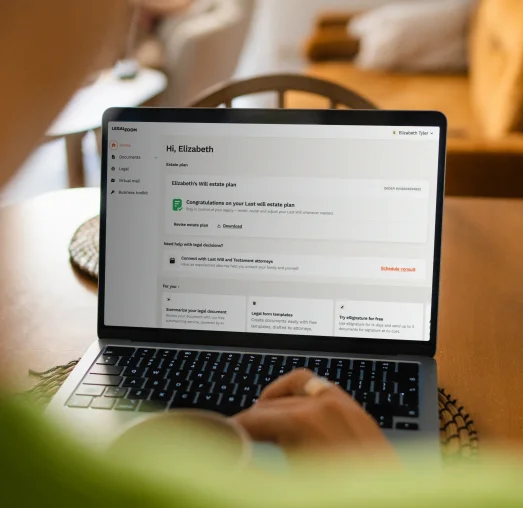 A person sits at a table with a laptop displaying a webpage titled "Hi, Elizabeth," showing details about a will and estate plan, while holding a cup