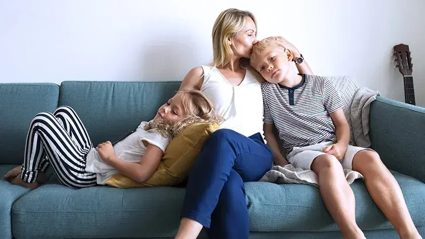 A mother sits on the sofa holding her kids.