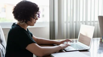 Woman in black top typing on a laptop near a window