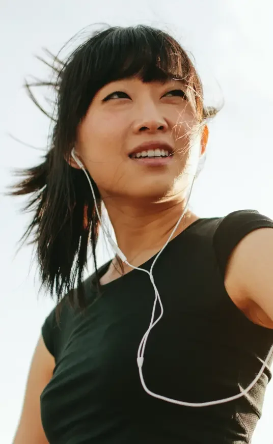 An asian woman looks onto the horizon in workout gear while listening to headphones.