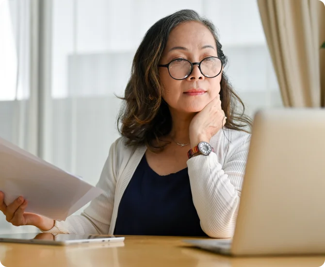 A black woman wearing a brown business suit has a discussion over paperwork with a client.