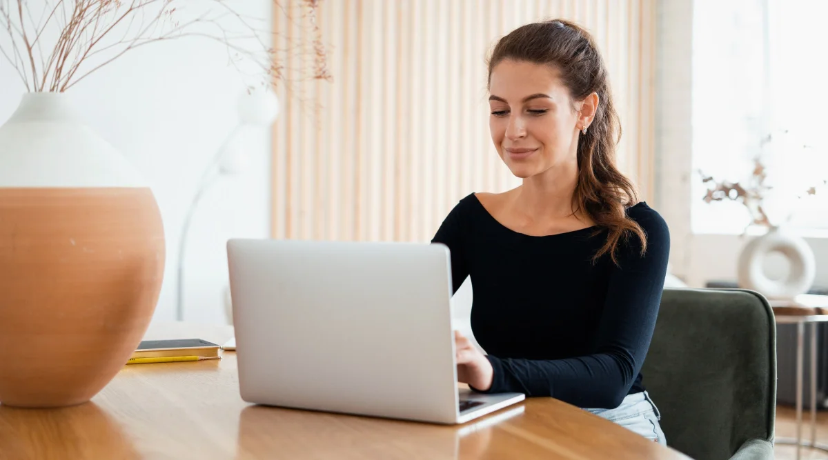 Woman smiling while typing on a laptop at a tabl