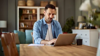 Man typing on a laptop in a home office setting