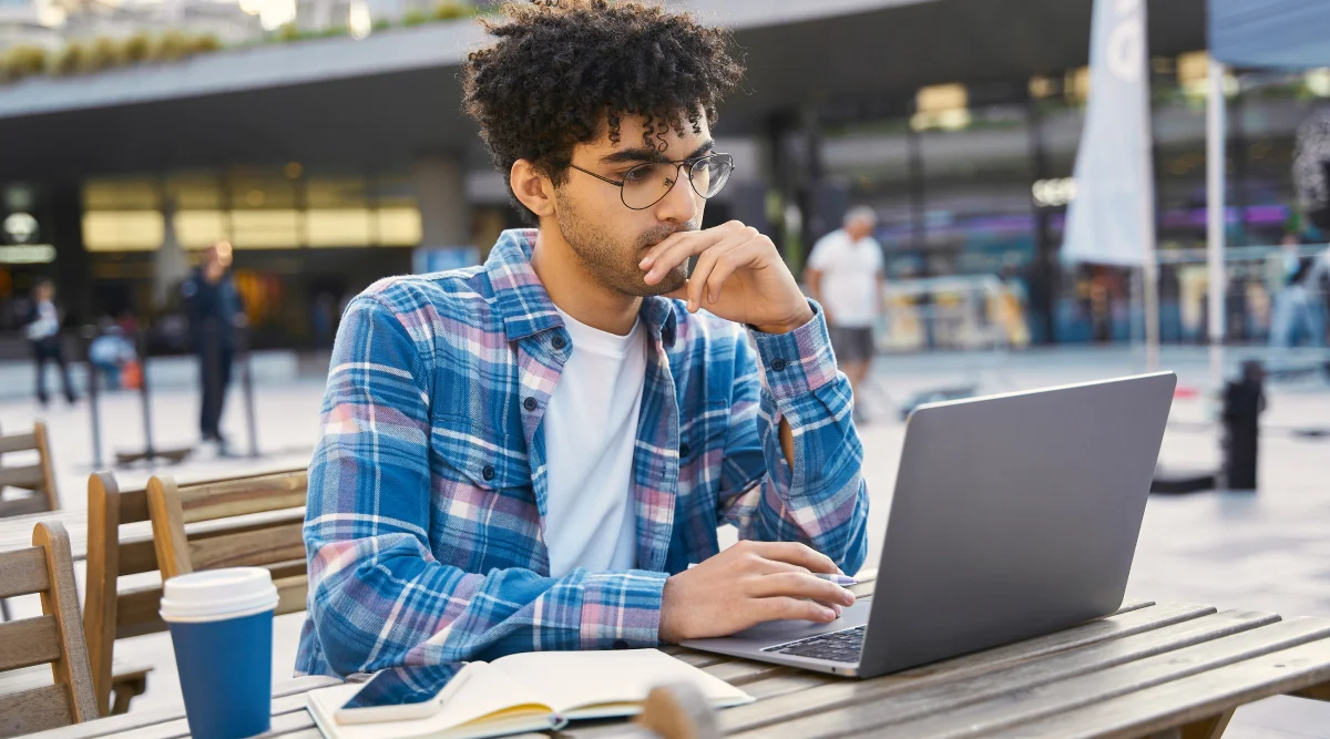 Man in a blue shirt working on a laptop outdoors