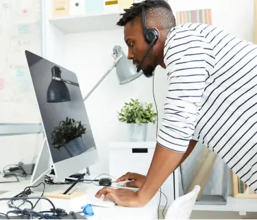 Black man wearing a black and white striped shirt. Wearing a headset and standing in front of his desktop in his home office after incorporating his business with LegalZoom.