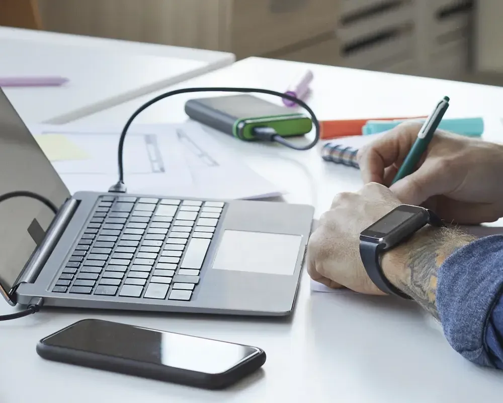 A photo of someone's hands taking notes on a cluttered office desk. 