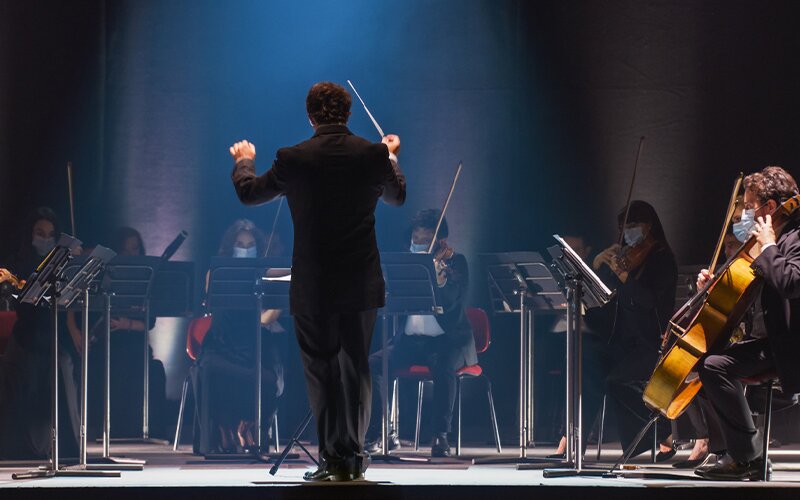 An image of an ongoing concert led by a conductor. 