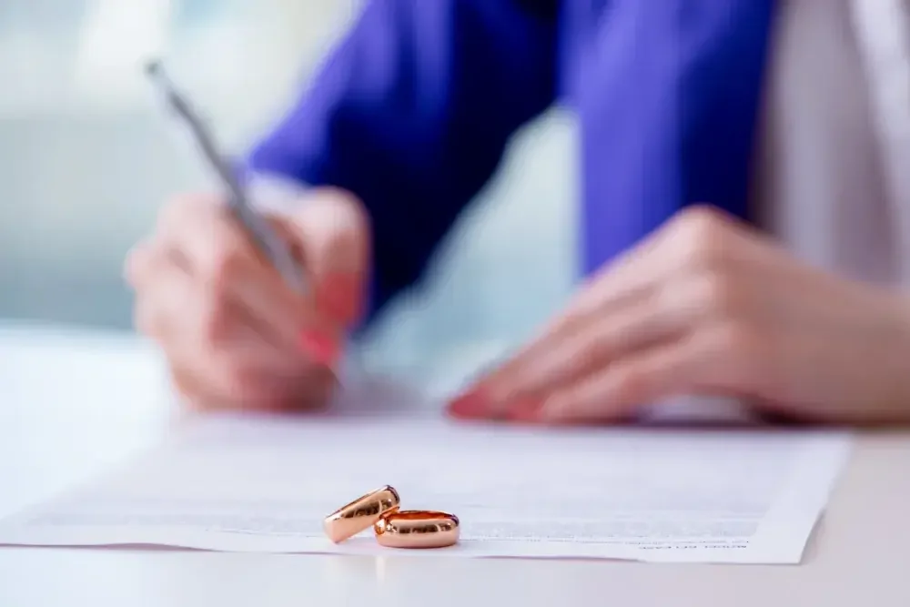 Close up of a pair of hands signing a divorce decree with wedding rings in the foreground.