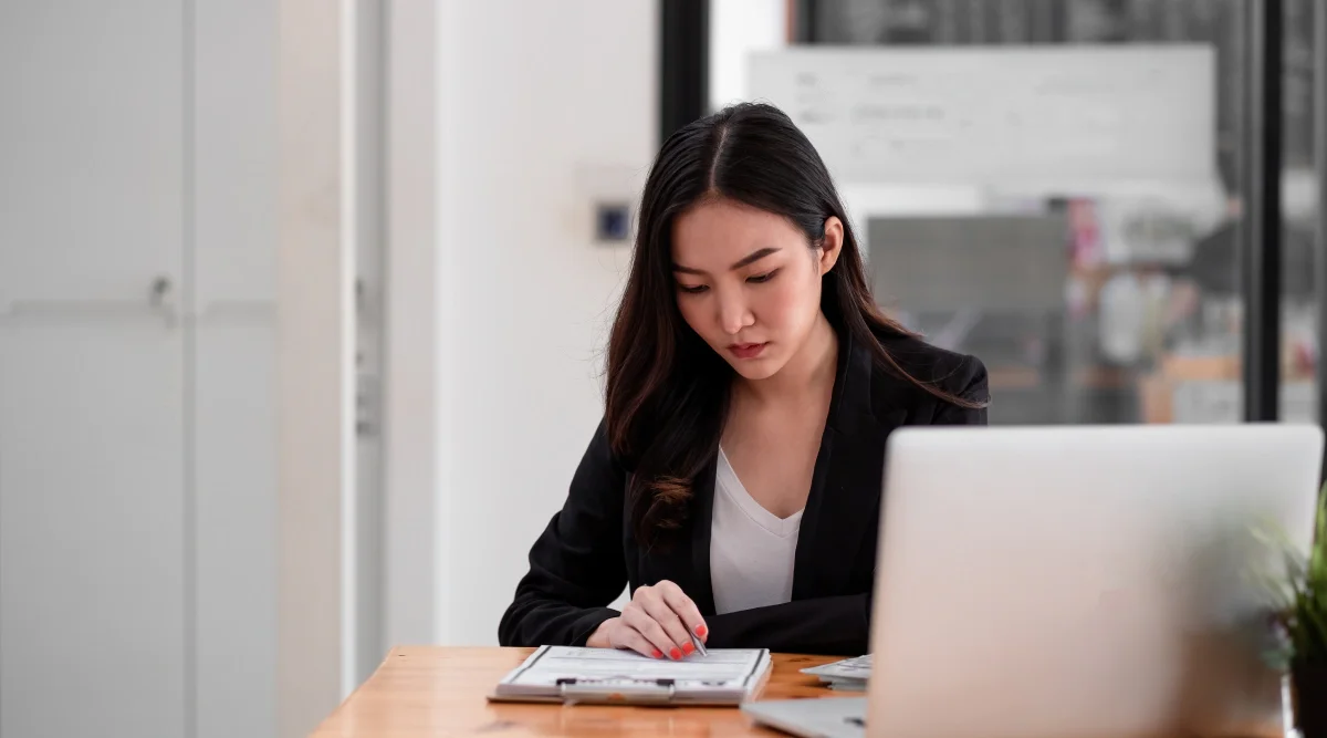 Woman working intently on papers beside a laptop in an office