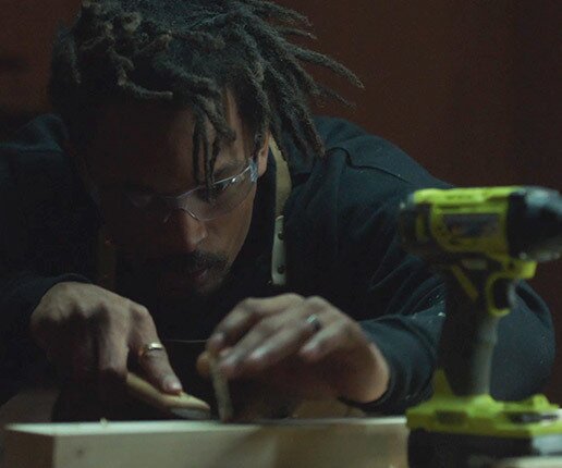 A man with pencil in his ear, wearing a construction toolbelt and operating a power sander.