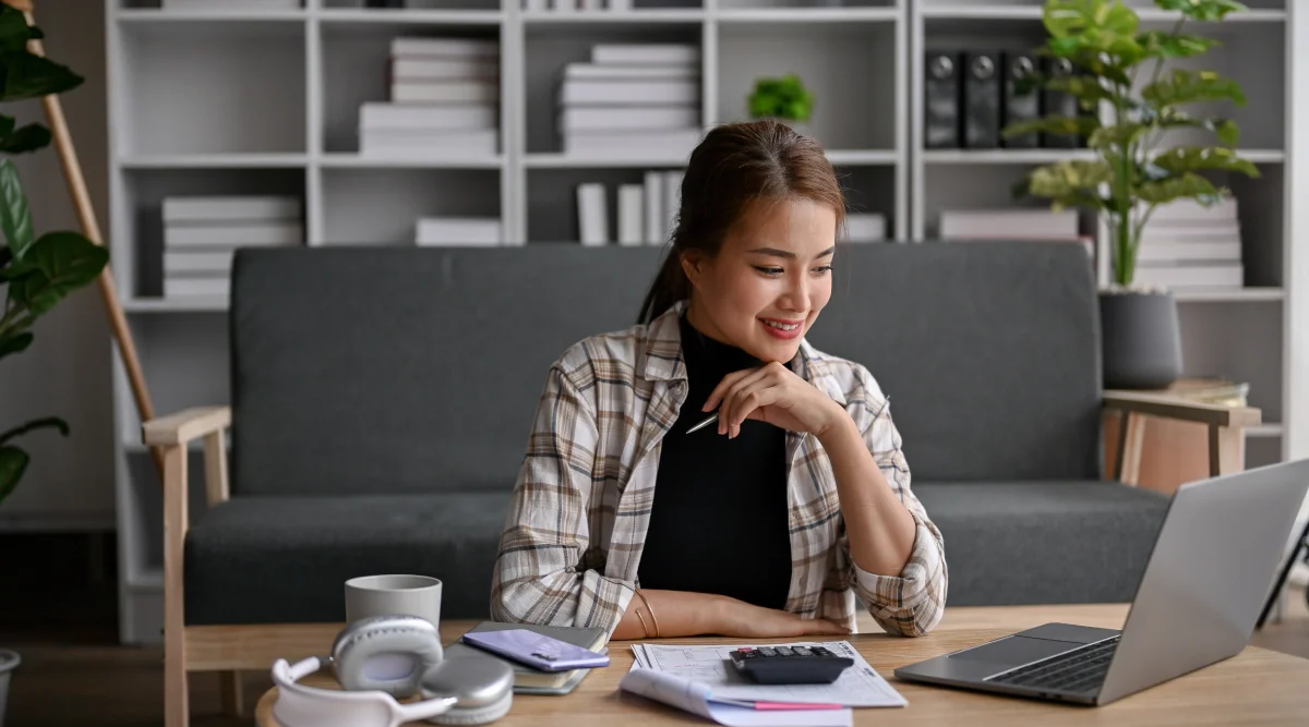 Woman smiling at a laptop with paperwork nearby