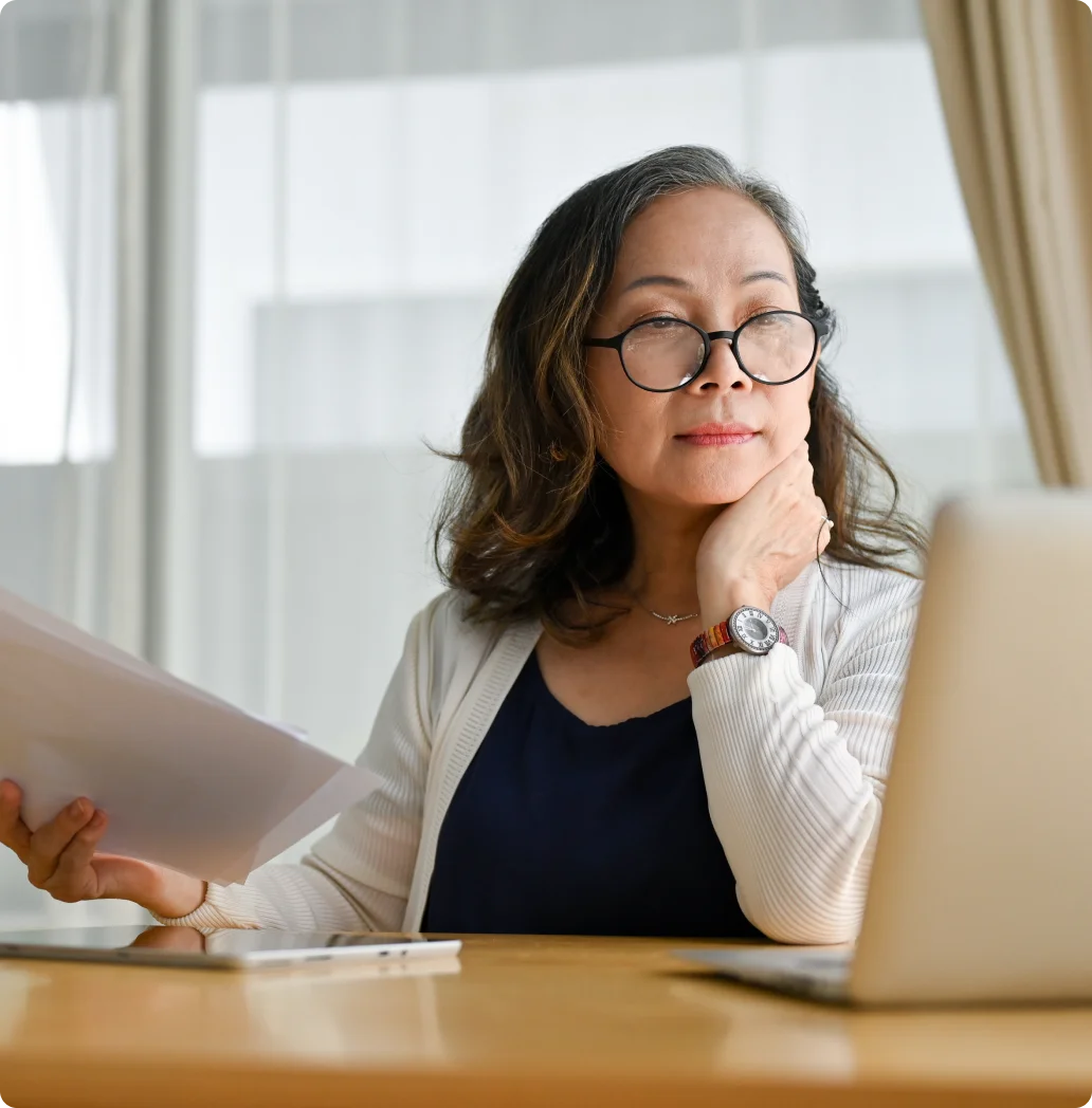 A woman wearing glasses sits at her computer thoughtfully