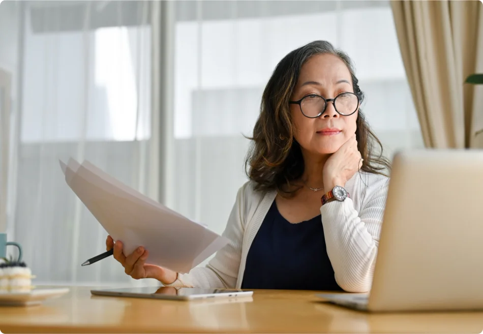 A woman wearing glasses sits at her computer thoughtfully.