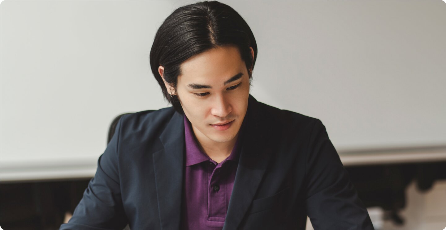 Asian man wearing a black suit jacket over a purple collared shirt working on his LegalZoom business dissolution on his laptop.