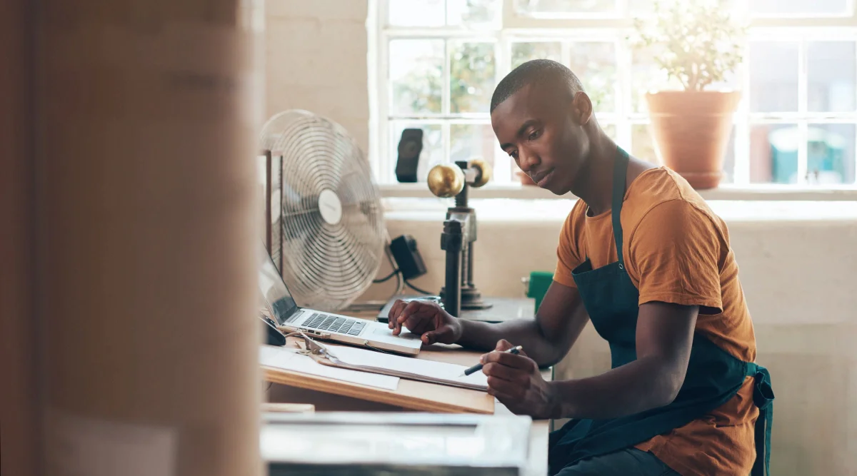 Man in apron working at a desk with a fan nearby