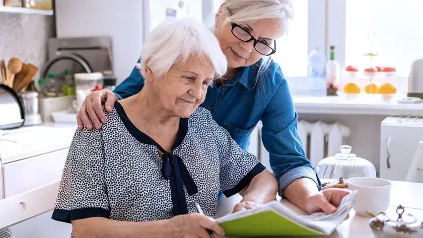 An elderly mother and adult daughter look over documents.