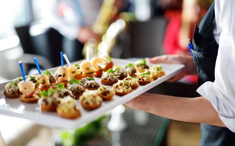 An image of a restaurant waiter serving food on a tray to their customers.