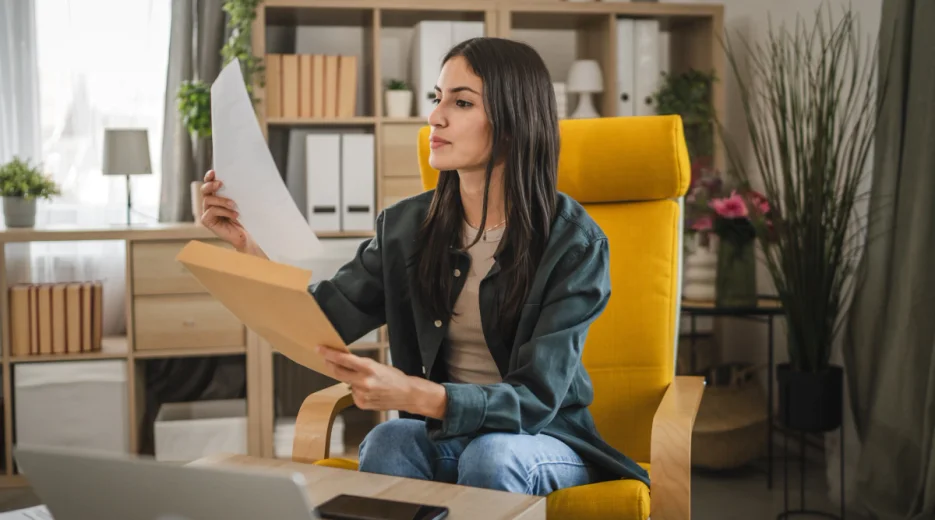 A woman sits at a desk reviewing an emergency power of attorney document with an open laptop nearby.