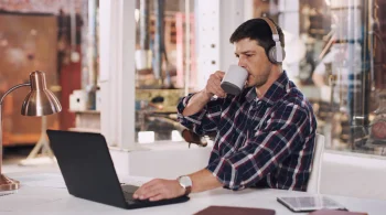 Man in headphones drinking coffee while using lapto