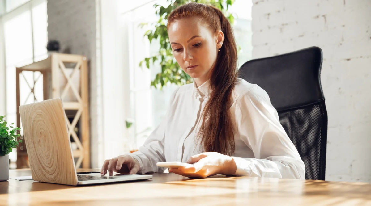 Woman in white shirt using laptop and phone