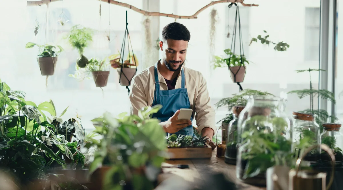 Man in apron using phone, surrounded by lush plants