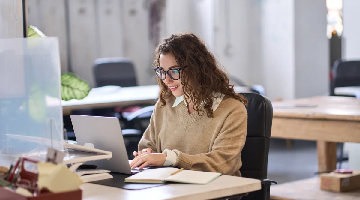 Woman working on a laptop smiling in an office setting