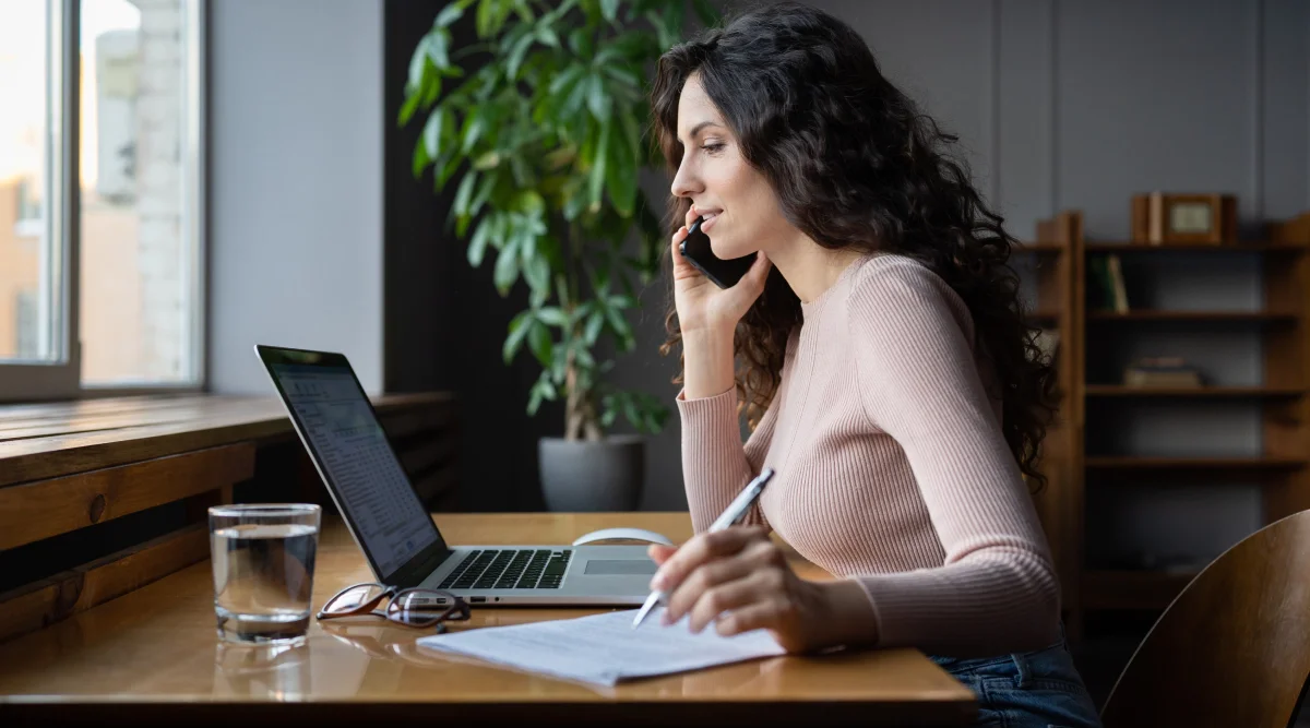 Woman on a phone call, writing notes at a desk