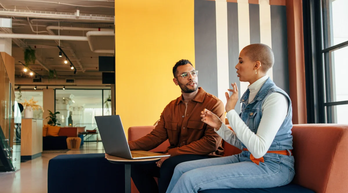 Two people discussing at a table with a laptop in a modern space