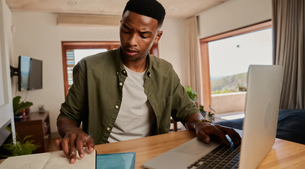 A man reviewing notes while working at his laptop.