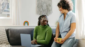 Two friends smiling while sitting with a laptop