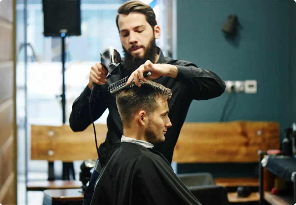 a hair stylist uses a blow dryer and brush for his client in a barber shop.