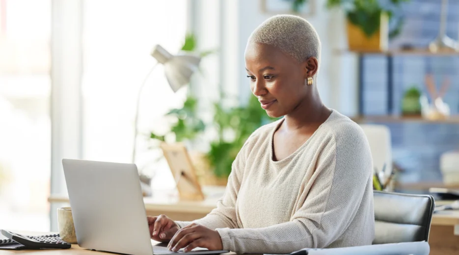 A woman sits at her desk and uses her laptop to research whether she needs a living trust or a will as part of her estate planning.