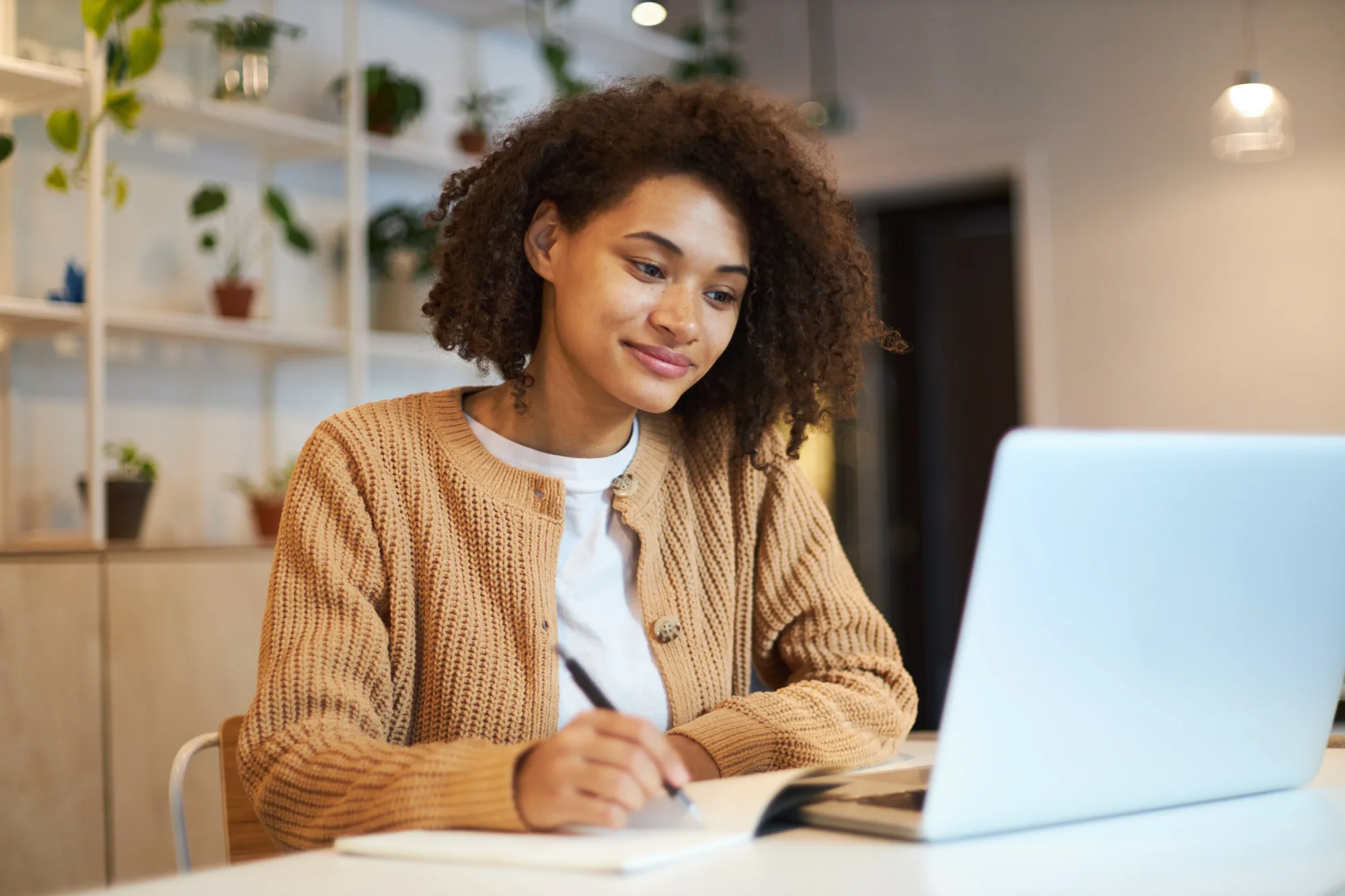 Woman in orange sweater with white shirt looks at her computer and smiles