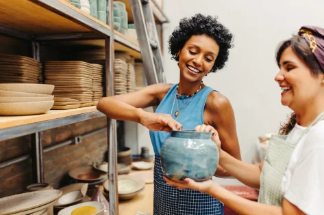 a woman holds a clay pot and another woman's hands hold the bottom.