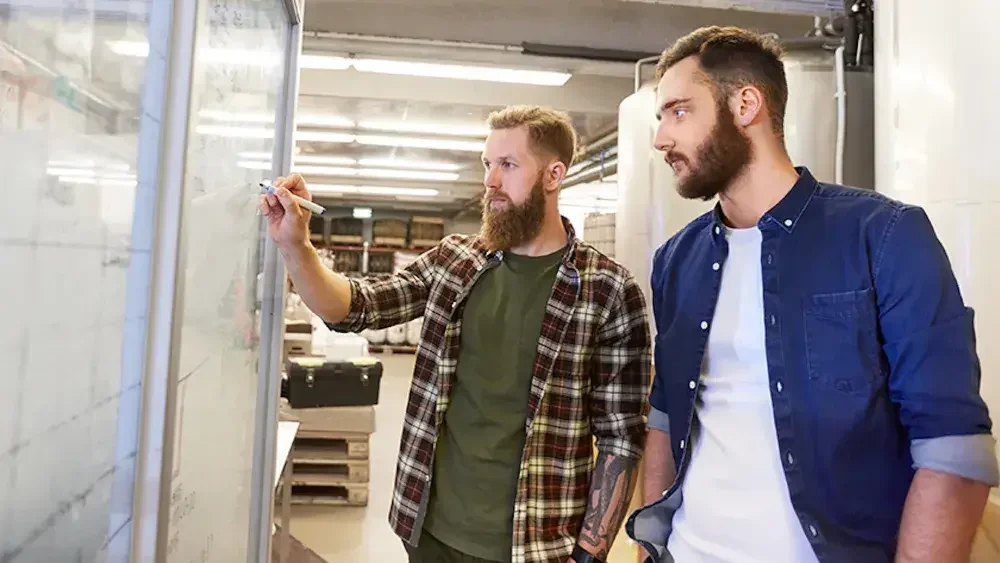 Two Florida business partners stand at a white board and work on their LLC's business plan.