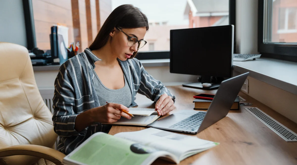 Woman studying with books and a laptop by a window