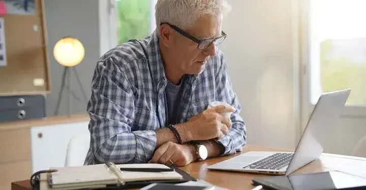 An elderly man is reading about the pros and cons of having a co-executor on his laptop.