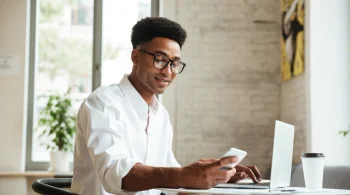 Man using a phone and laptop in a bright office