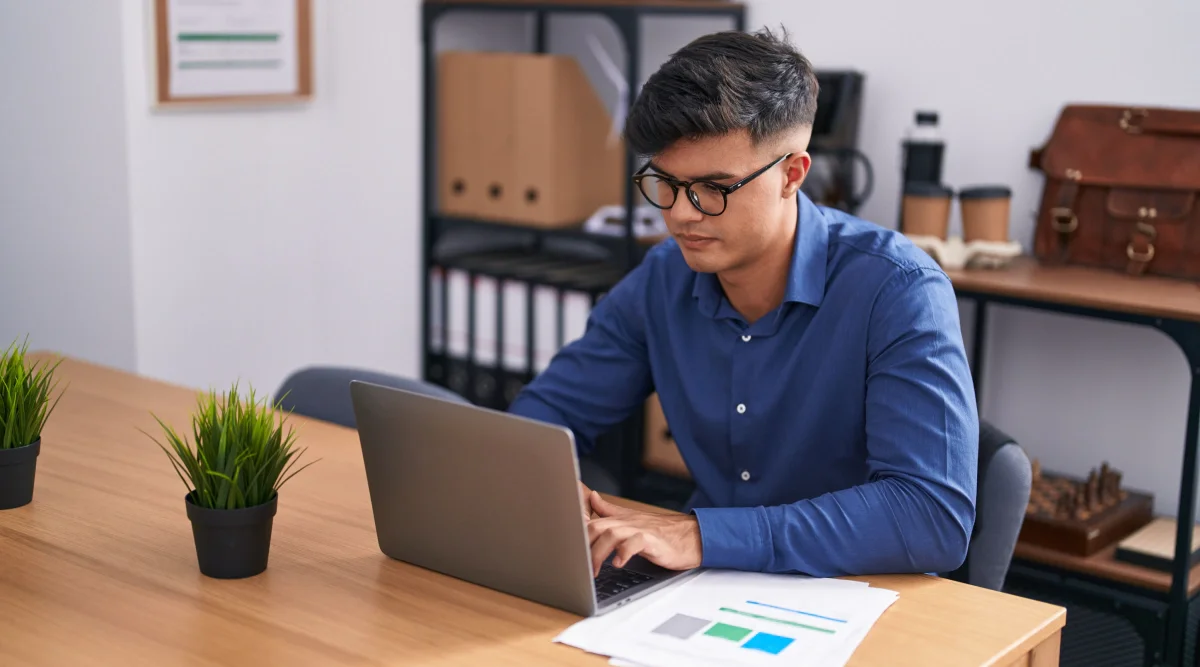 Man in blue shirt focused on laptop with papers